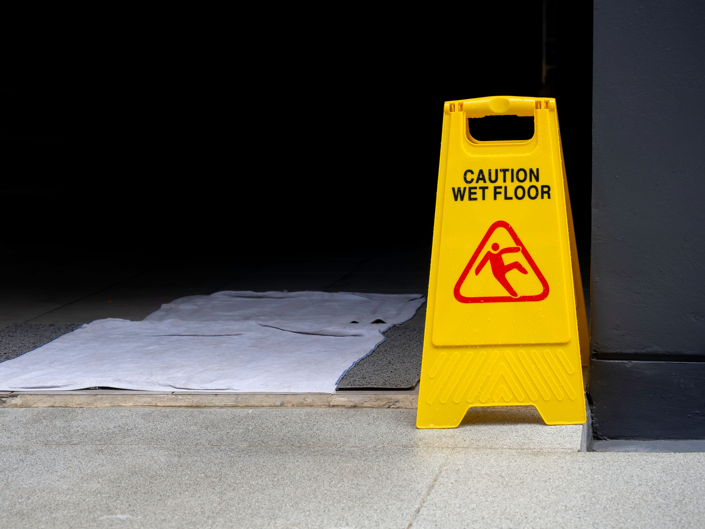 Wet floor caution sign on walkway near the building after raining. Warning yellow plastic caution wet floor sign on the ground with copy space.